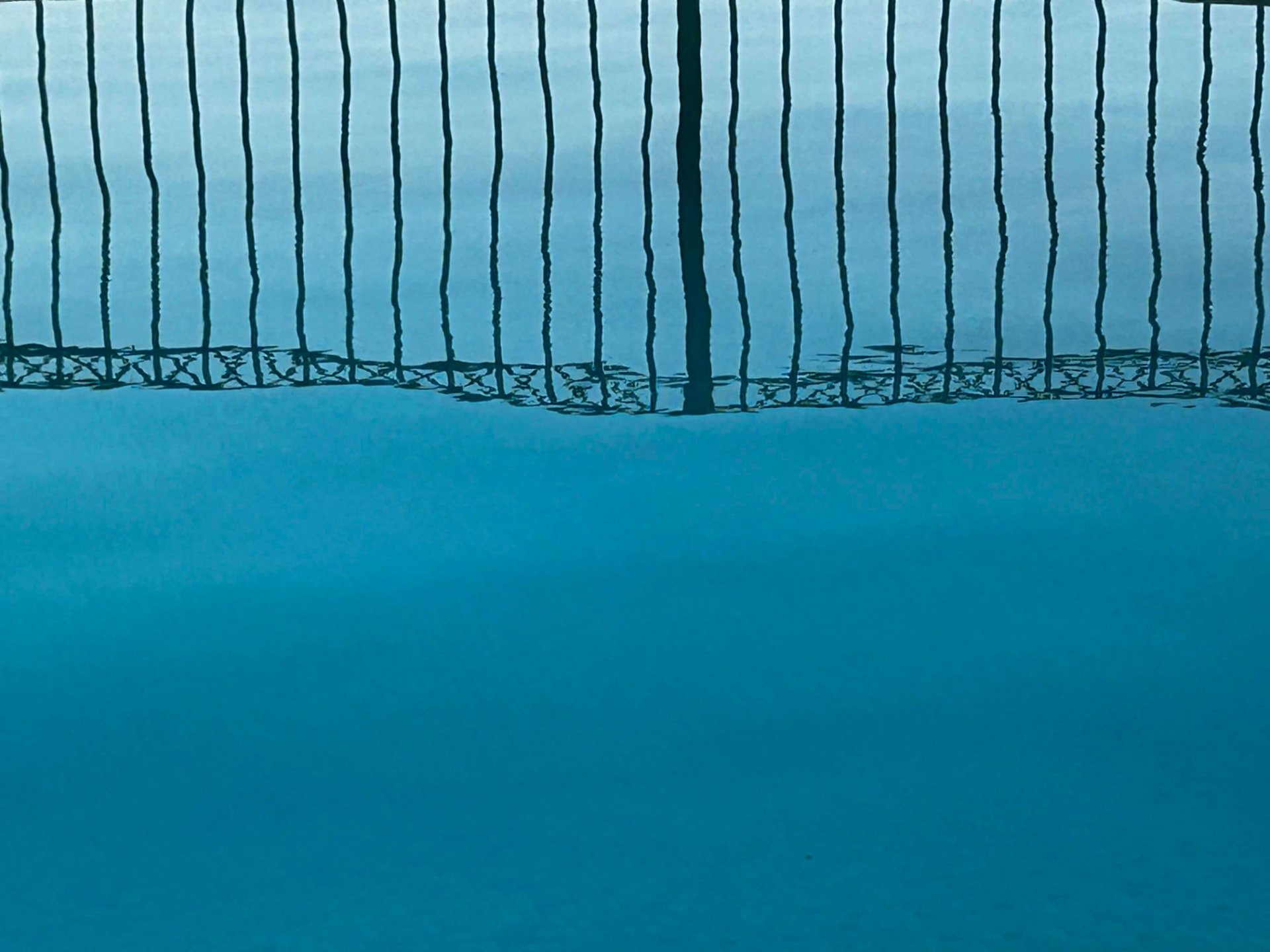 Dark vertical reflections wavering across clear blue water